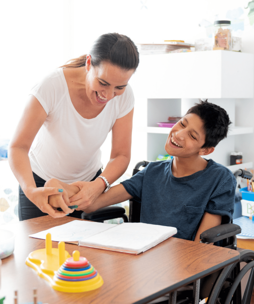 Cerebral palsy support aid assisting a child holding a pen. The boy has cerebral palsy and is sitting in a wheelchair