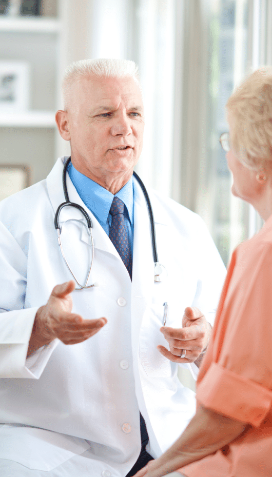 Older male doctor sitting with a female patient, discussing surgery