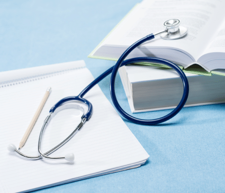 Stethoscope laying on top of a notebook and medical books