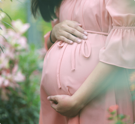 Close up of the belly of a pregnant woman in a pink dress holding her stomach.