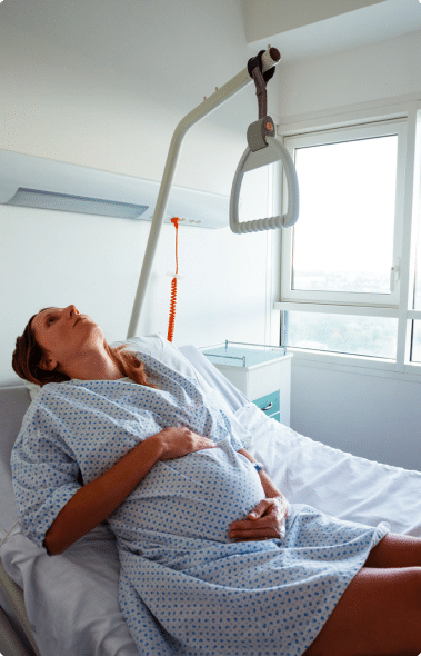Pregnant woman in a bright hospital room, holding her stomach.