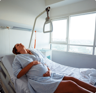 Pregnant woman in a bright hospital room, holding her stomach.