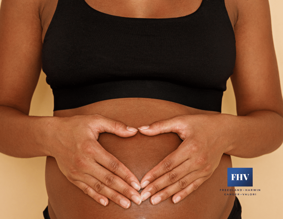 Black mother holding her hands in a heart shape on her pregnant abdomen